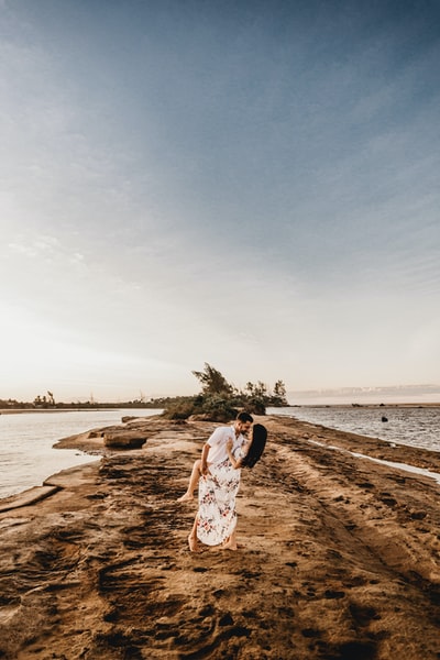 妇女在白色和棕色裙子站在棕色沙附近的水域白天
